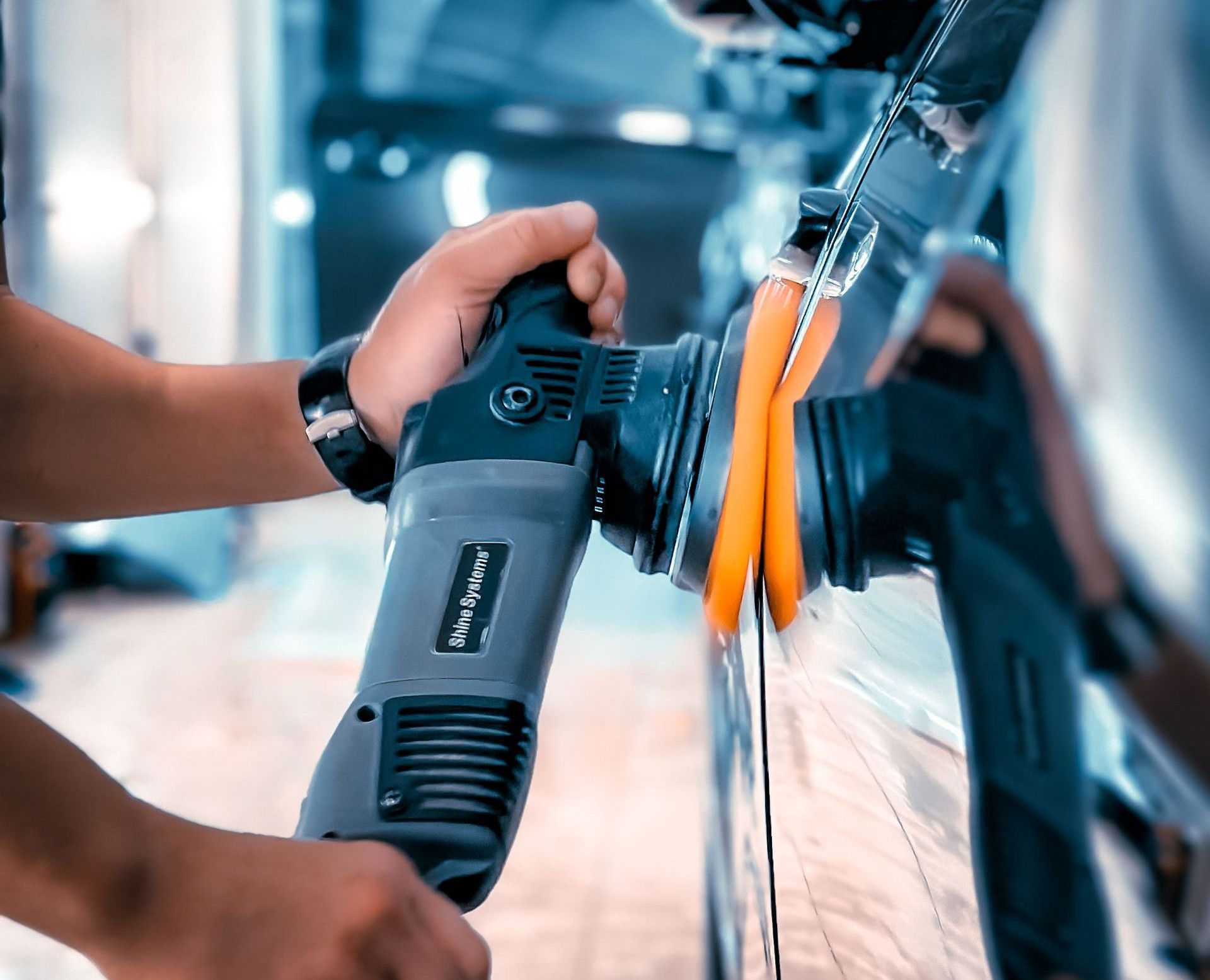 Close-up of a man polishing a car in a garage using an electric buffer tool, showcasing car maintenance.