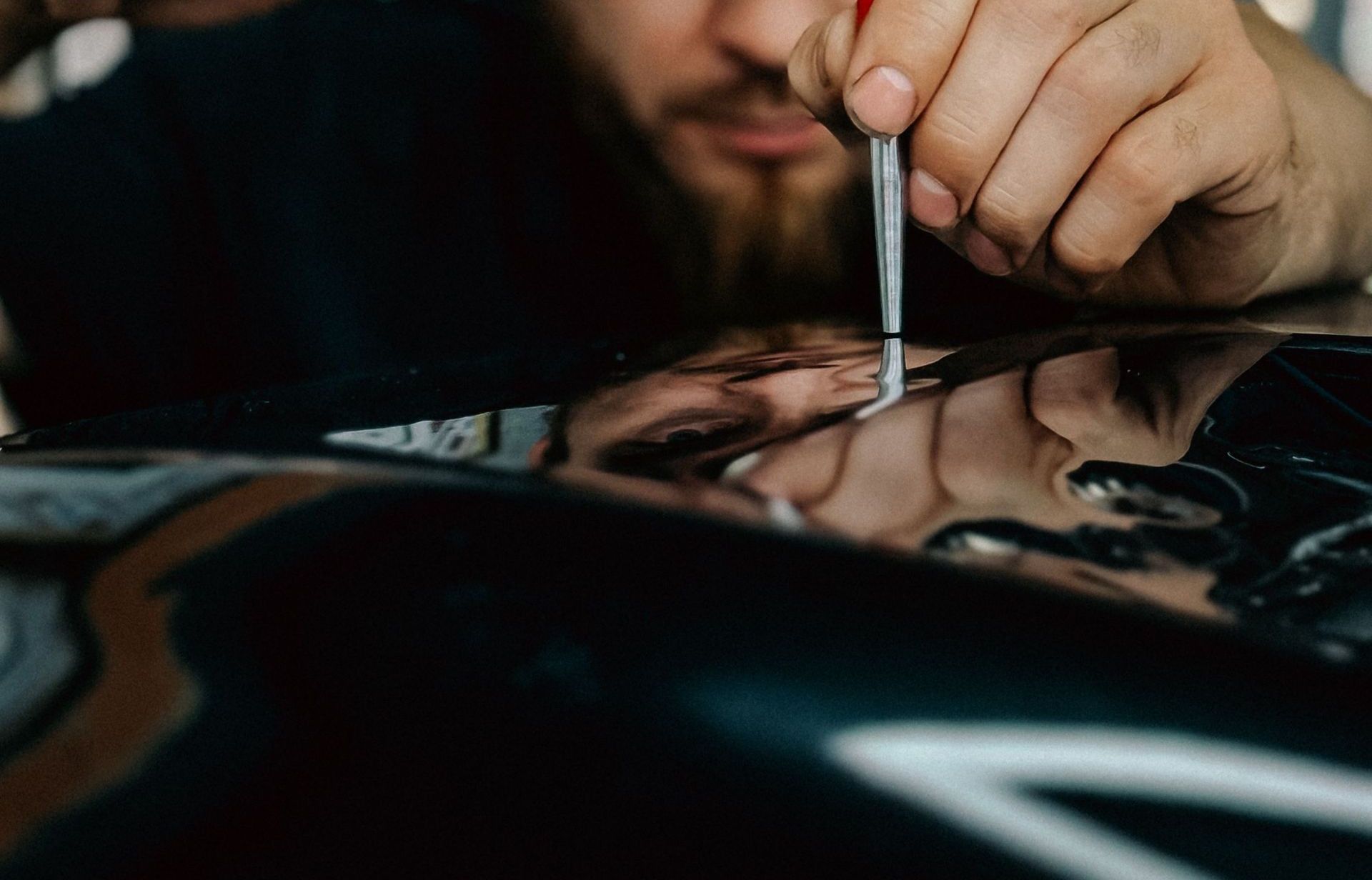 Mechanic expertly repairing car dent using specialized tool in workshop.